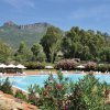 Piscina circondata da ombrelloni, montagne sullo sfondo.