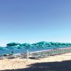 Spiaggia con ombrelloni verdi e lettini.