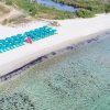 Ombrelloni verdi su spiaggia di sabbia bianca vista dall'alto.