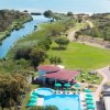 Piscina circondata da ombrelloni, fiume e giardino sullo sfondo.