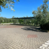 Parcheggio pavimentato con tettoia, circondato da alberi e cielo sereno.