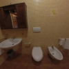Bagno con rivestimento a mosaico giallo, lavabo, WC, bidet e asciugamani appesi.