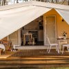 Tenda glamping con veranda, tavolo da pranzo e sedie.