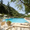 Una piscina all'aperto circondata da sedie e alberi, con persone rilassate sotto gli ombrelloni.