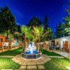 Un giardino notturno con fontana luminosa e bungalow illuminati, circondato da alberi.