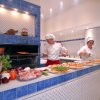 Due chef preparano pizze in una cucina con rivestimenti blu, con ingredienti freschi sul bancone.