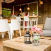 Area relax con tavolino in legno, lanterna e vasetto con fiori rosa, arredamento moderno.