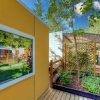 Giardino con terrazza in legno, piante e strutture moderne sotto un cielo azzurro.