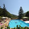 Piscina all'aperto con persone che nuotano, circondata da lettini e ombrelloni.