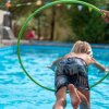 Bambino salta attraverso un cerchio verde verso una piscina.