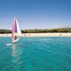Windsurf in mare turchese vicino a una spiaggia sabbiosa.