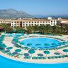 Piscina circolare con ombrelloni verdi, hotel sullo sfondo.