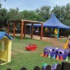 Parco giochi con casetta, scivolo e tenda blu.
