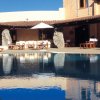 Piscina con sedie a sdraio e ombrelloni bianchi di fronte a un edificio con grandi rocce decorative.