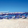 Una spiaggia con sedie a sdraio blu, ombrelloni e una rete da pallavolo di fronte al mare.
