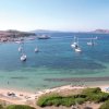 Spiaggia sabbiosa con barche a vela in mare e bagnanti sulla riva.