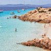 Spiaggia rocciosa con acqua cristallina e persone che nuotano e si rilassano.