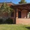 Esterno di una casa con veranda coperta, pareti rosa e prato con palme.