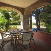 Veranda con tavolo e sedie sotto archi in pietra, circondata da alberi e vegetazione.