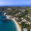 Vista aerea di una costa collinare con spiaggia sabbiosa e acque blu.