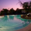 Una piscina illuminata al tramonto, circondata da palme.