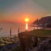 Un tramonto sul mare con ombrelloni gialli e una terrazza verde. Le colline si intravedono a destra.