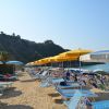 Spiaggia con sdraio e ombrelloni gialli e bianchi, vista mare e scogliera.
