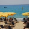 Spiaggia con ombrelloni gialli, lettini e mare blu con barca e windsurf.