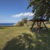 Un ampio giardino con altalena e vista sul mare, circondato da alberi.