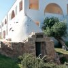 Edificio bianco con archi, giardino e trullo in pietra.