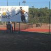 Campo da tennis con rete e cartellone promozionale.