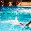 Nuotatore in piscina, persone sedute sul bordo.