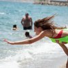 Donna in spiaggia si china verso il mare.