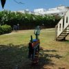 Parco giochi erboso con giochi a molla e scivolo vicino a una siepe.
