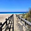 Una passerella di legno conduce a una spiaggia con sabbia e mare azzurro.