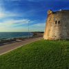 Una torre di pietra accanto a una strada costiera, con il mare sullo sfondo.