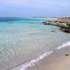Spiaggia di sabbia chiara con acque limpide e onde leggere.