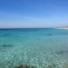 Mare cristallino e spiaggia sabbiosa sotto un cielo blu.