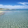 Spiaggia sabbiosa con mare cristallino e cielo blu.