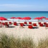 Ombrelloni e lettini rossi su una spiaggia sabbiosa con mare blu.