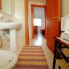 Bagno con lavabo bianco, asciugamani e tappeto colorato, vista su camera da letto.